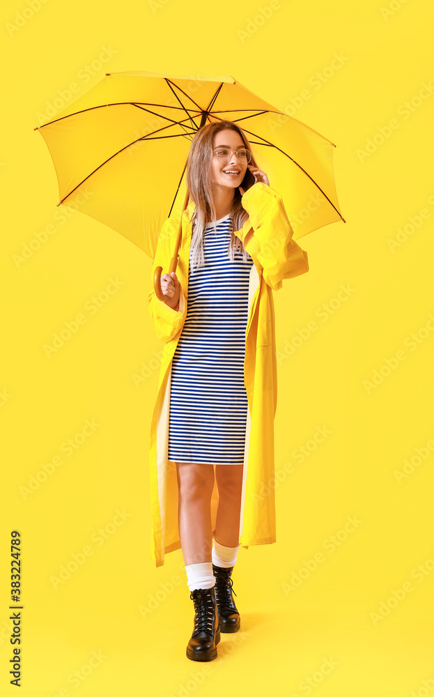 Beautiful young woman in raincoat and with umbrella on color background