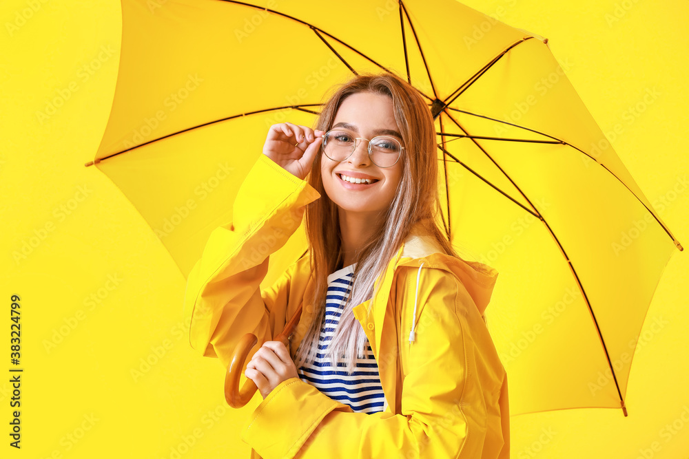 Beautiful young woman in raincoat and with umbrella on color background