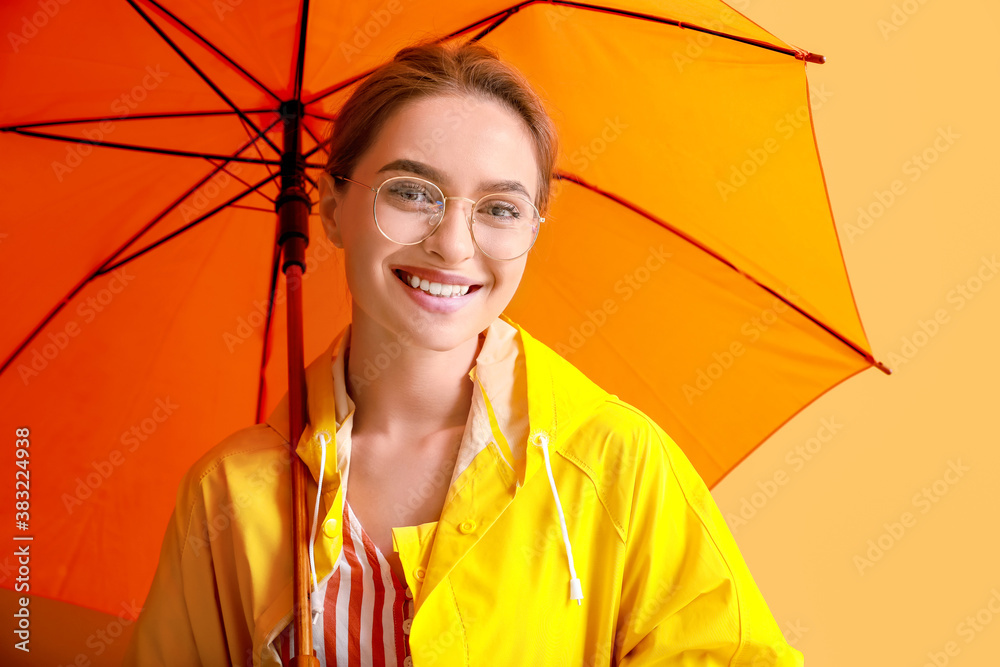 Beautiful young woman in raincoat and with umbrella on color background