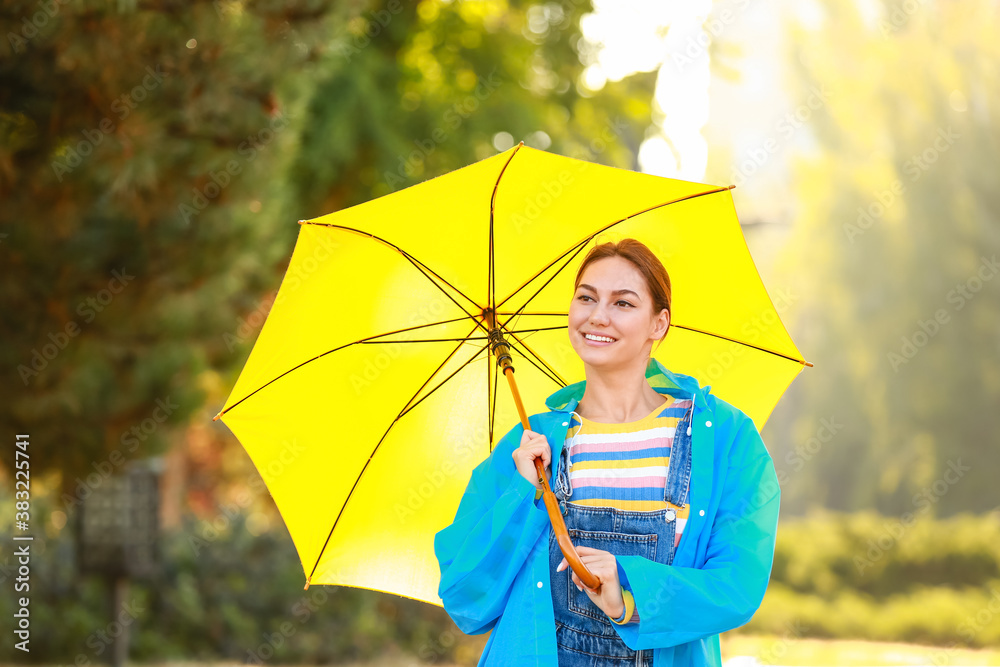 美丽的年轻女子在公园里打着雨伞，穿着雨衣