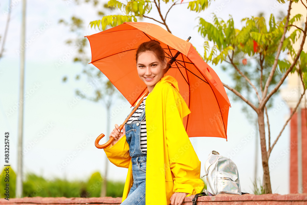 Beautiful young woman with umbrella wearing raincoat outdoors