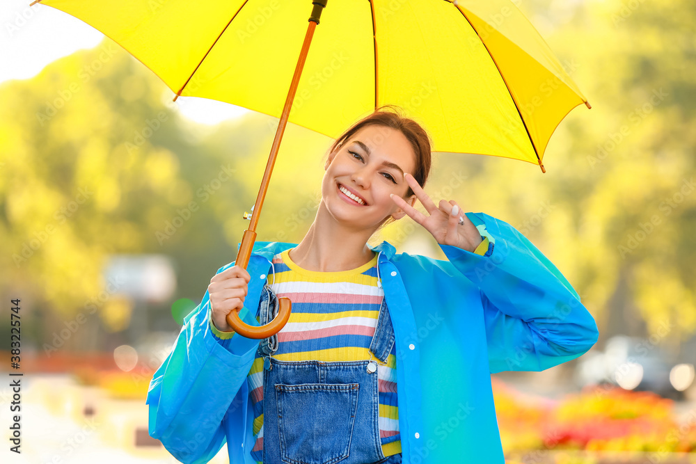 Beautiful young woman with umbrella wearing raincoat in park