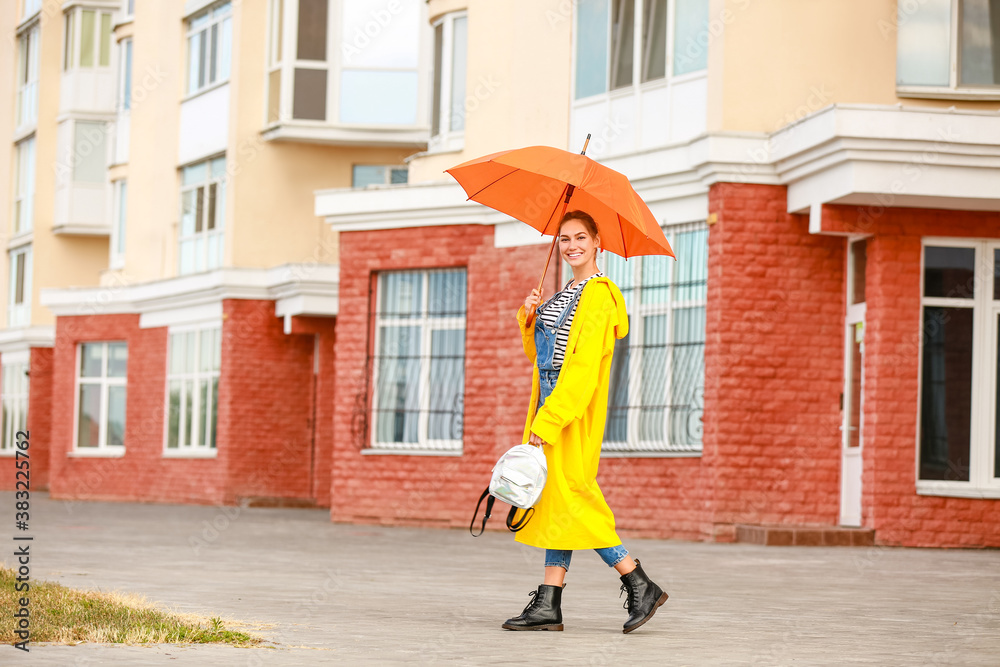 Beautiful young woman with umbrella wearing raincoat outdoors