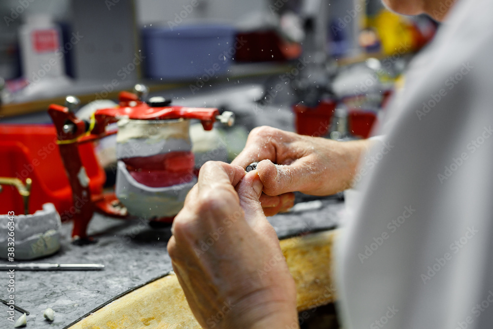 Dental technician working on artificial tooth using special dental tools.