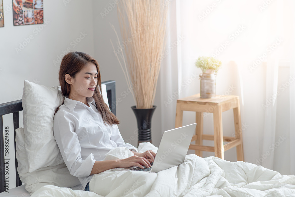 Young Asian woman relaxing and lying in bed at home with use the laptop computer in bedroom