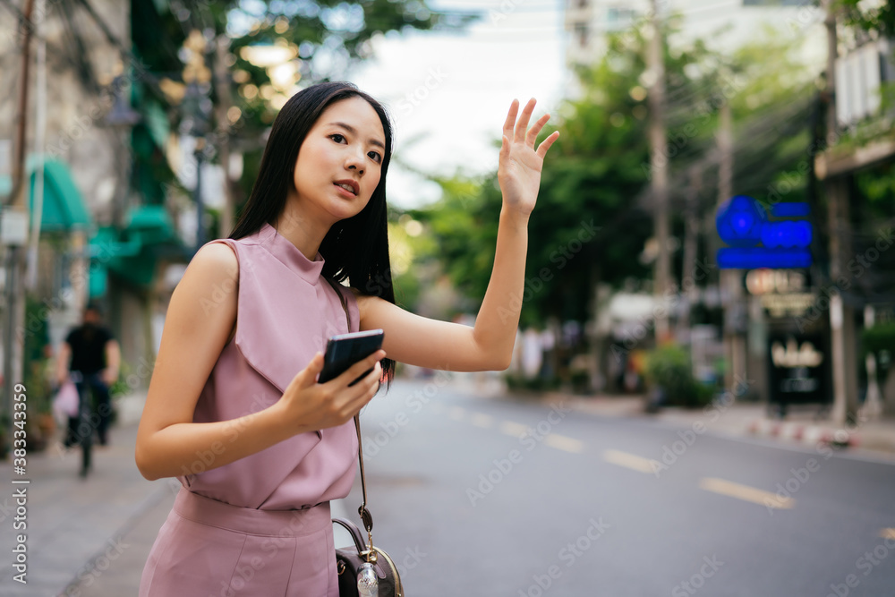 Happy Asian businesswoman on side of road holding smartphone, using app to book a cab, communication