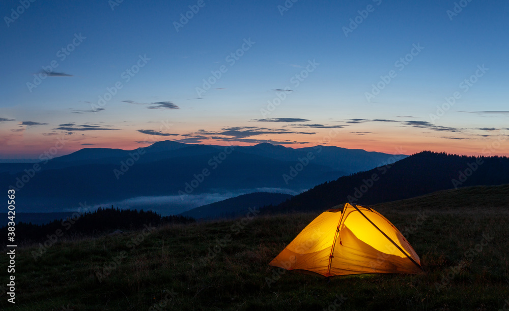 Orange luminous tent on the mountain in evening or early morning