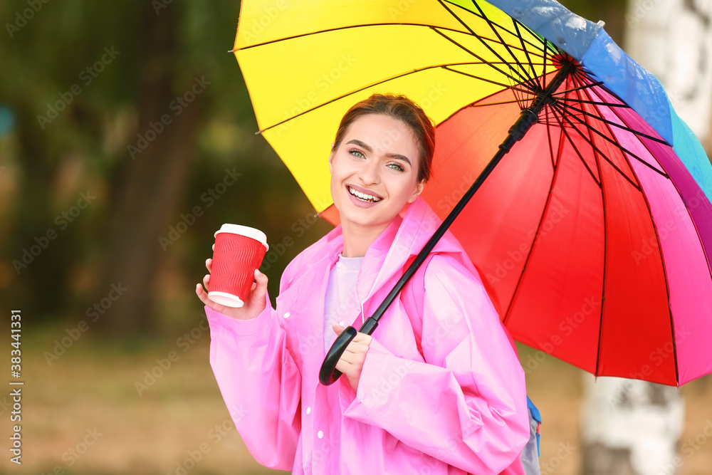 Beautiful young woman with umbrella and coffee wearing raincoat outdoors