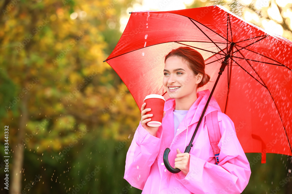 Beautiful young woman with umbrella and coffee wearing raincoat outdoors