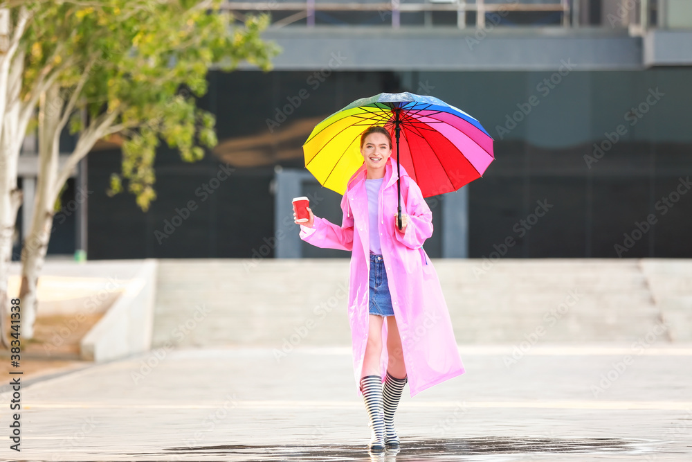 Beautiful young woman with umbrella and coffee wearing raincoat outdoors