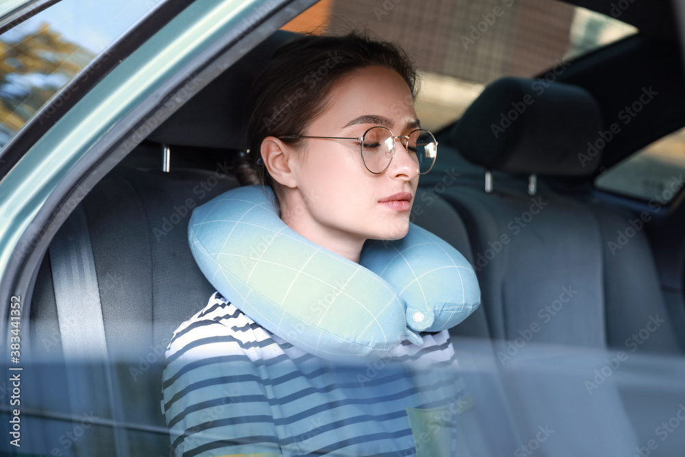 Beautiful young woman with travel pillow sitting in car