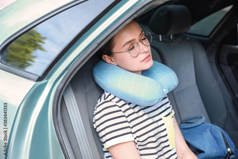 Beautiful young woman with travel pillow sitting in car