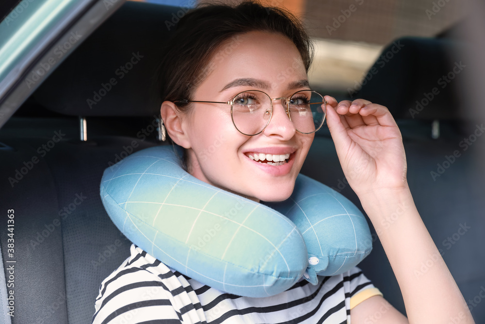 Beautiful young woman with travel pillow sitting in car