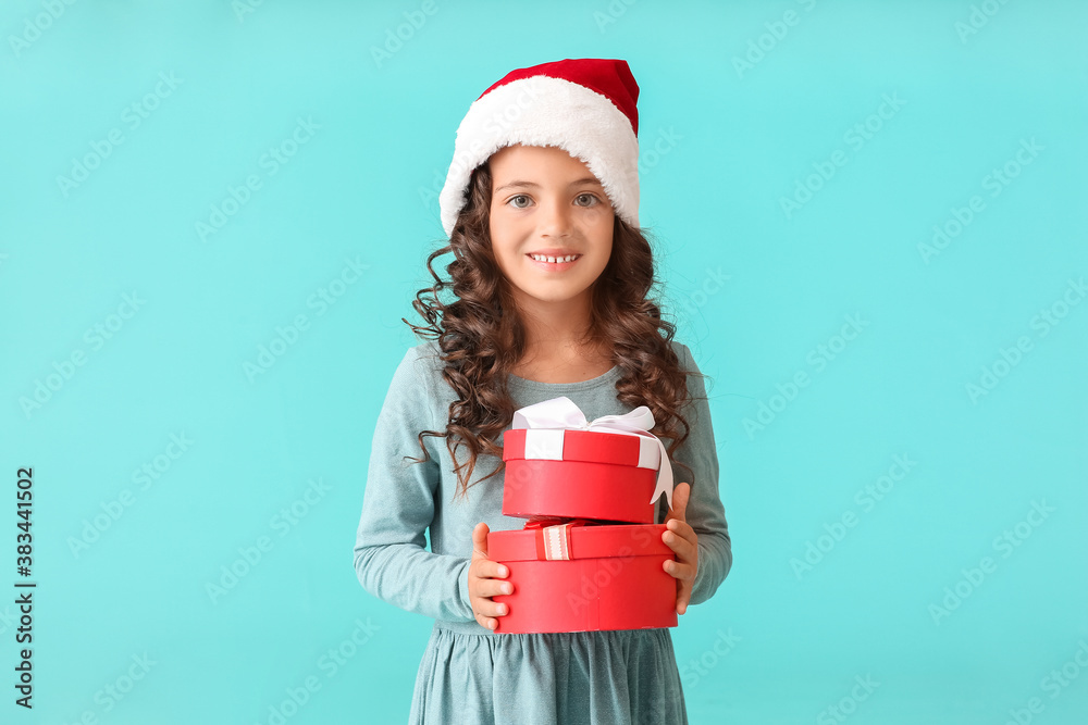 Cute little girl in Santa hat and with gift boxes on color background