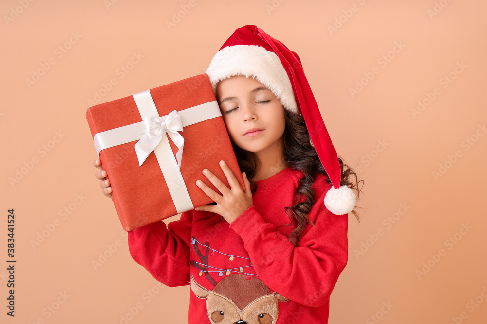 Cute little girl in Santa hat and with gift on color background