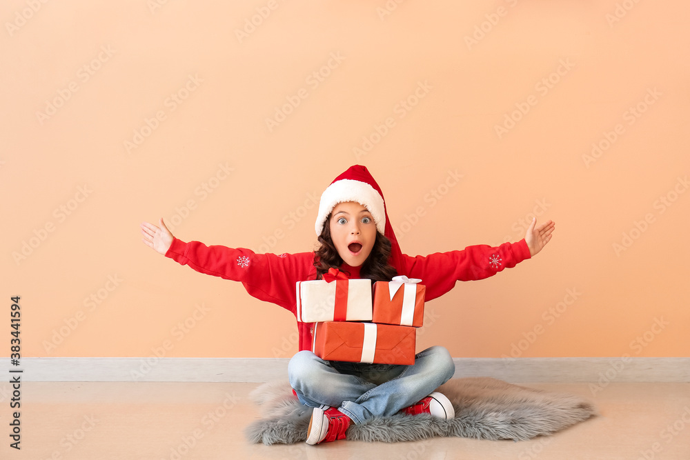 Surprised little girl in Santa hat and with gift boxes near color wall