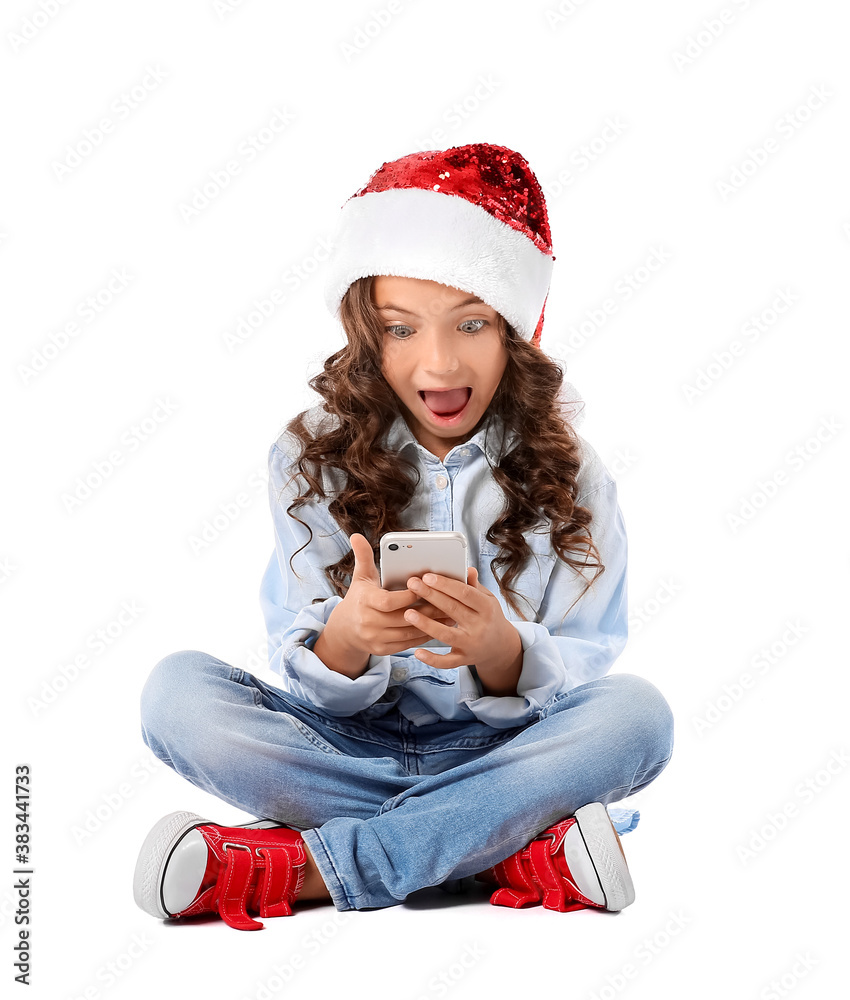 Cute little girl in Santa hat and with mobile phone on white background