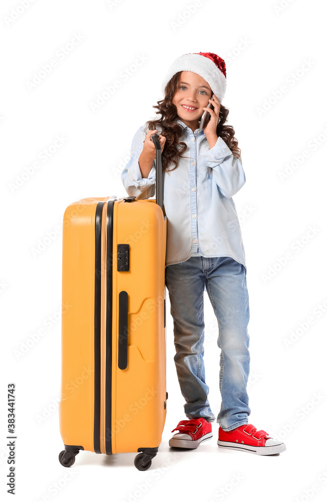 Cute little girl in Santa hat and with suitcase talking by phone on white background. Christmas vaca