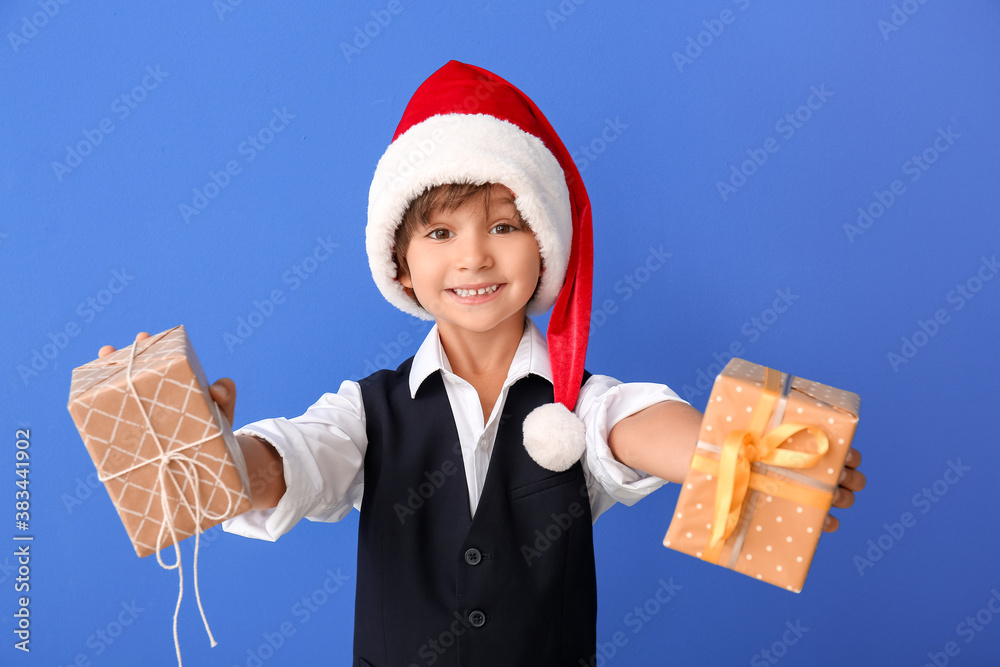 Cute little boy in Santa hat and with gift boxes on color background