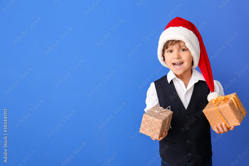 Cute little boy in Santa hat and with gift boxes on color background