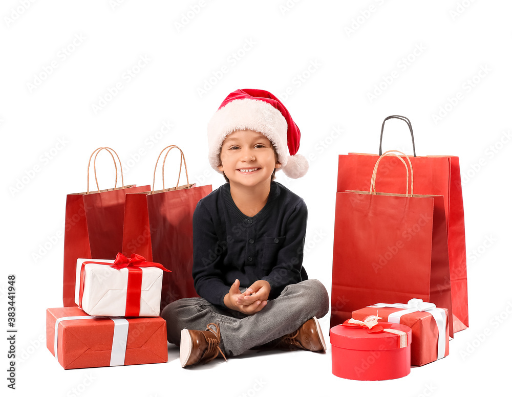 Cute little boy in Santa hat, with gift boxes and shopping bags on white background