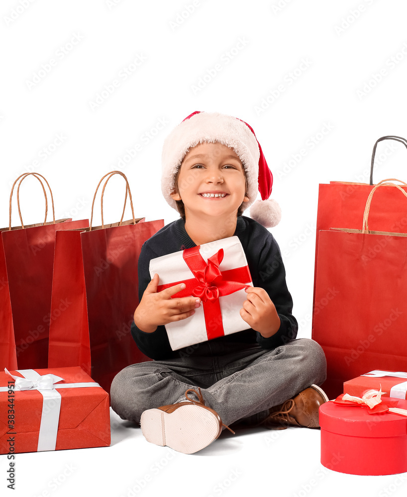 Cute little boy in Santa hat, with gift boxes and shopping bags on white background