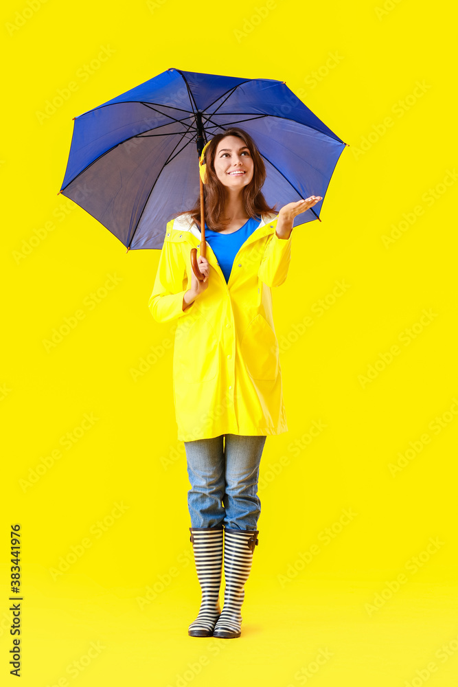 Beautiful young woman in raincoat and with umbrella on color background