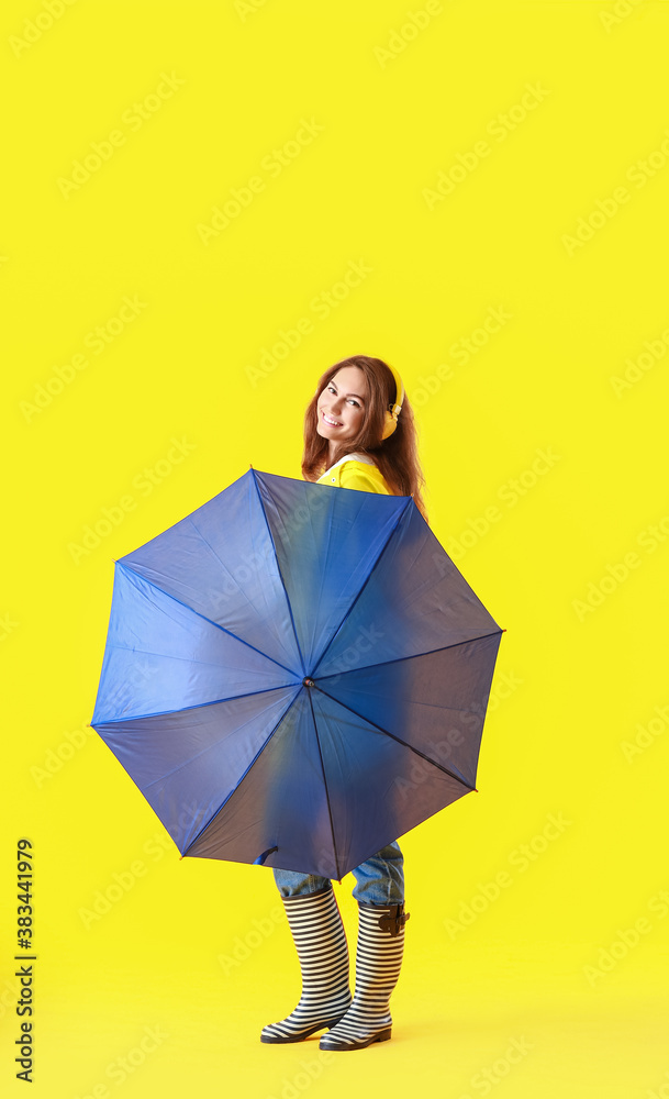 Beautiful young woman in raincoat and with umbrella on color background