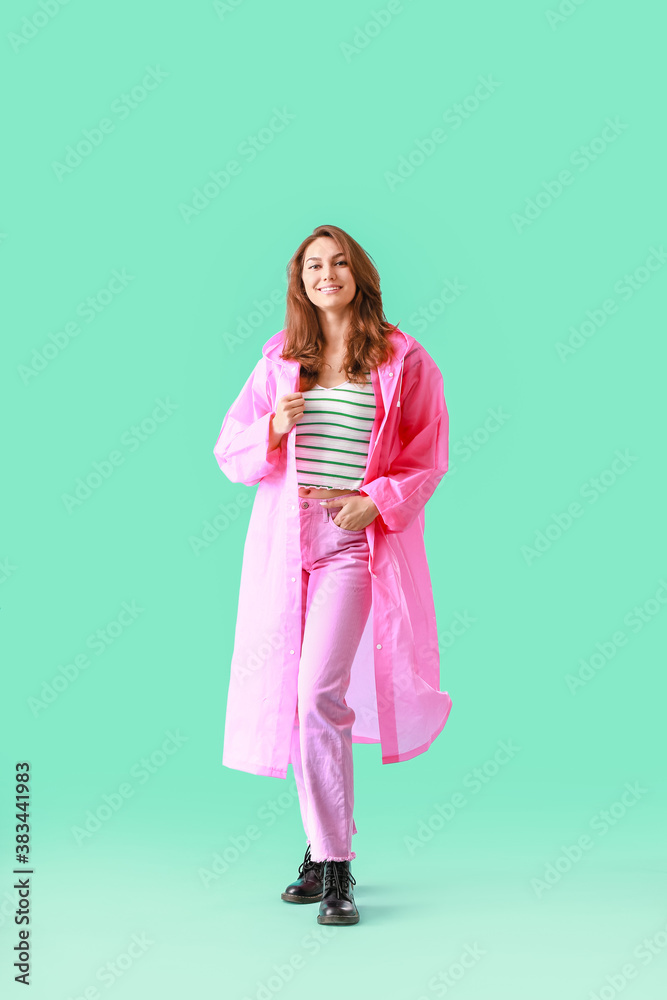 Beautiful young woman in raincoat on color background