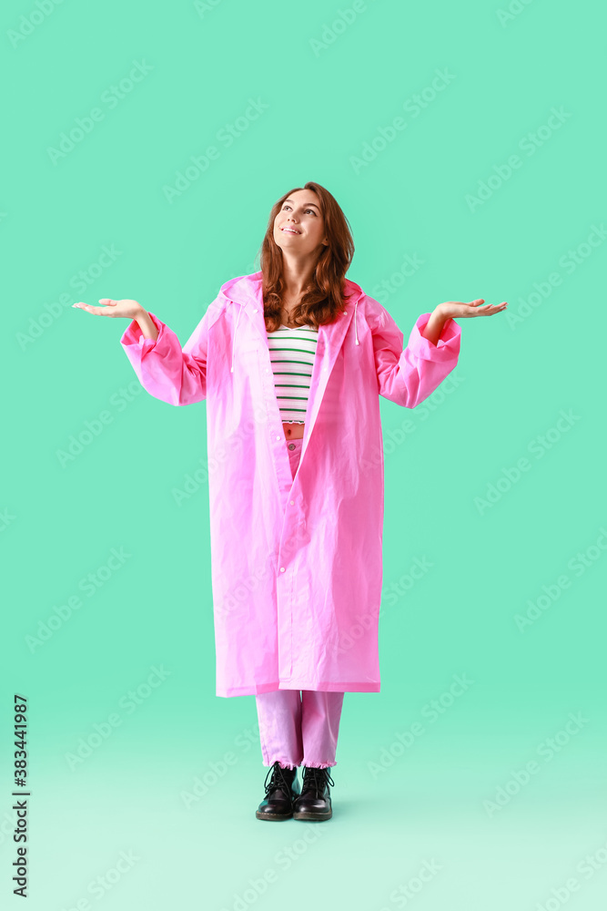 Beautiful young woman in raincoat on color background