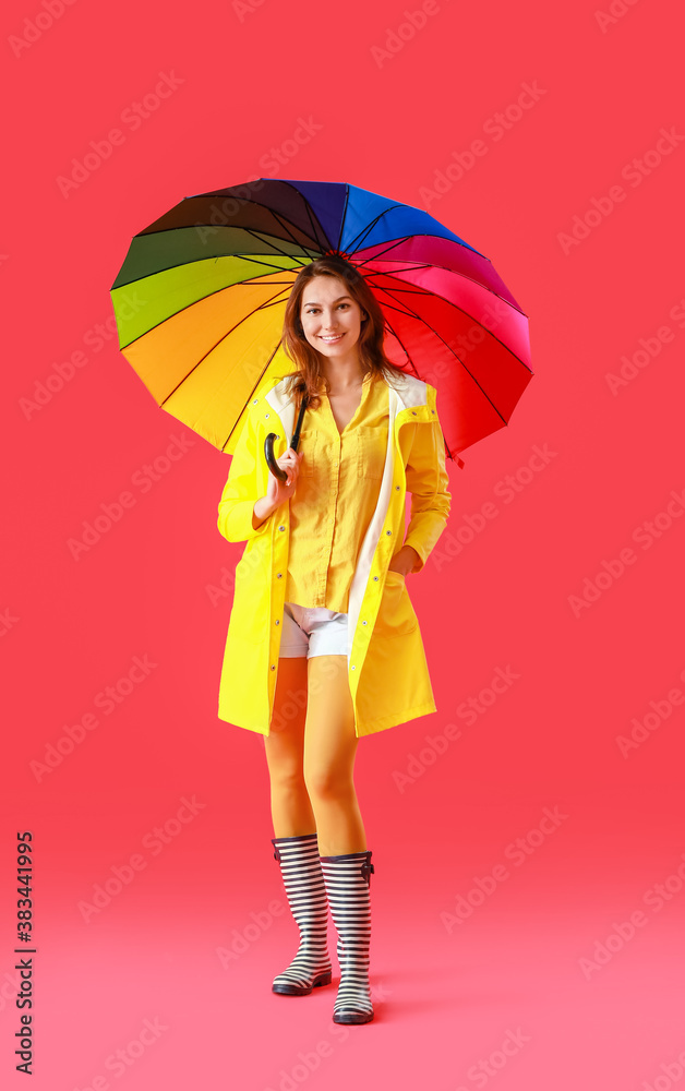 Beautiful young woman in raincoat and with umbrella on color background