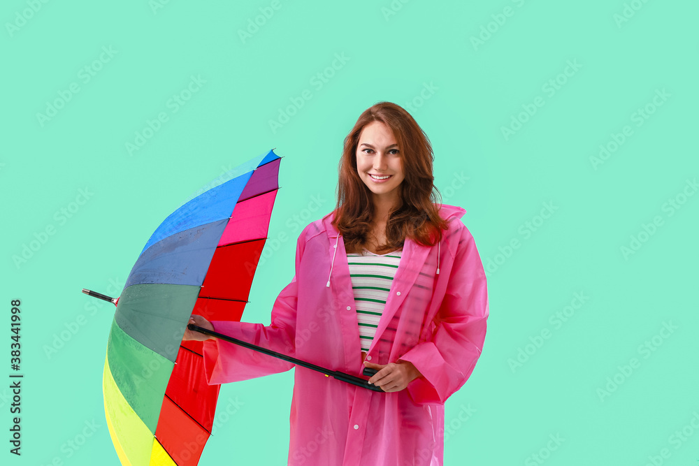 Beautiful young woman in raincoat and with umbrella on color background