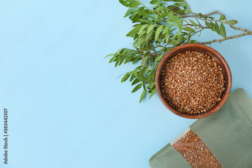 Bag and bowl with buckwheat groat on color background