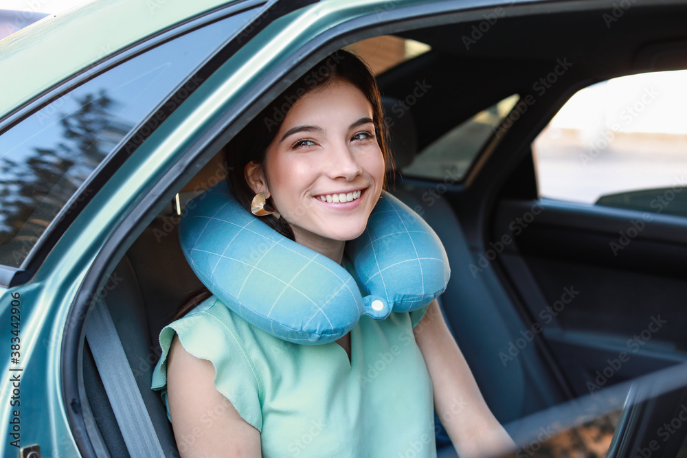 Beautiful young woman with travel pillow sitting in car