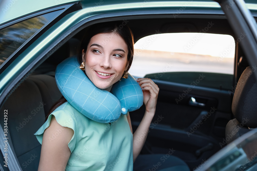 Beautiful young woman with travel pillow sitting in car