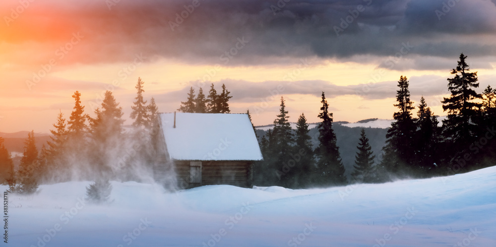 Fantastic winter landscape with wooden house in snowy mountains. Hight mountain peaks in foggy sunse