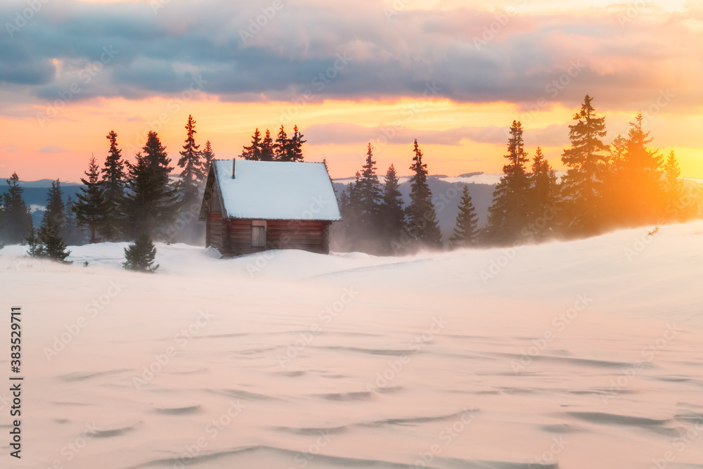 Fantastic winter landscape with wooden house in snowy mountains. Hight mountain peaks in foggy sunse