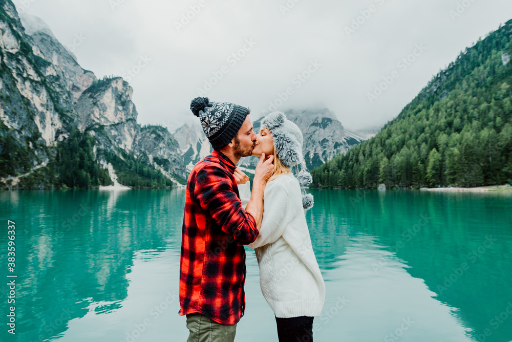 Romantic kiss of a couple of adults visiting an alpine lake at Braies Italy. Tourist in love spendin