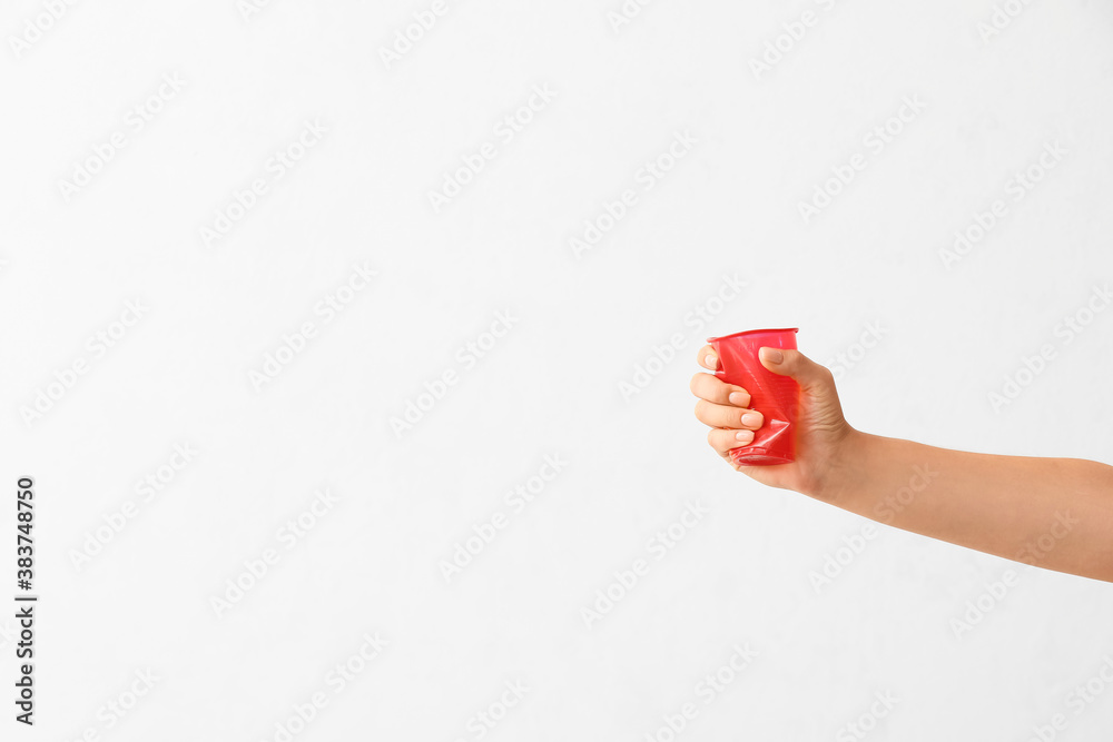 Female hand crumpling plastic cup on light background. Ecology concept