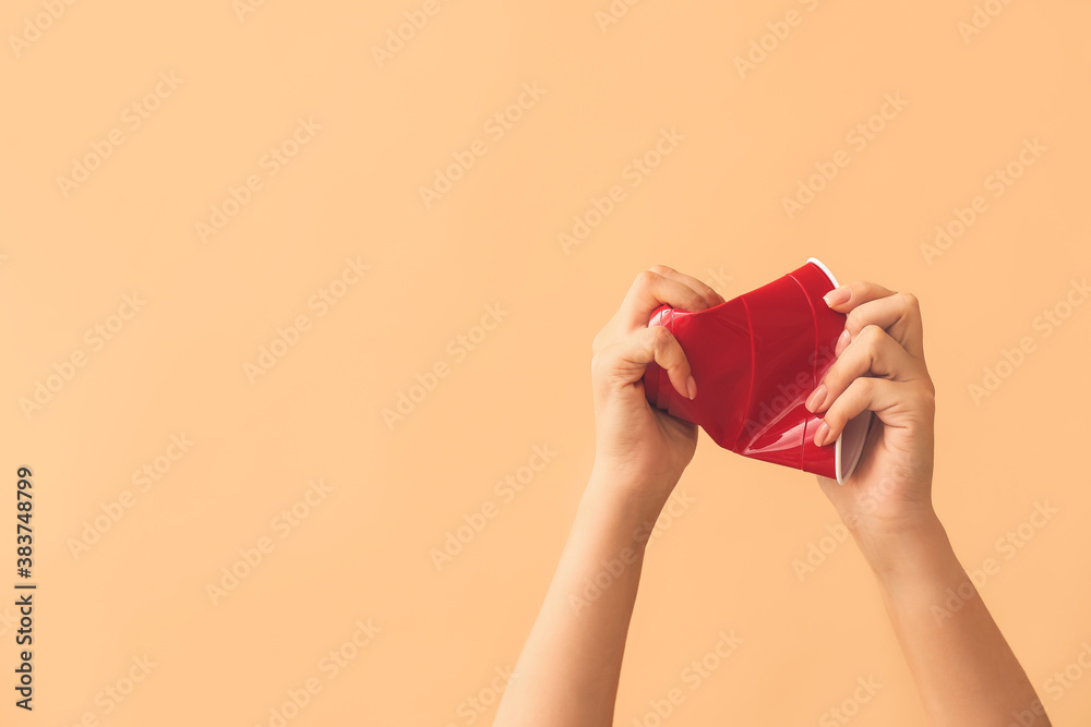 Female hands crumpling plastic cup on color background. Ecology concept