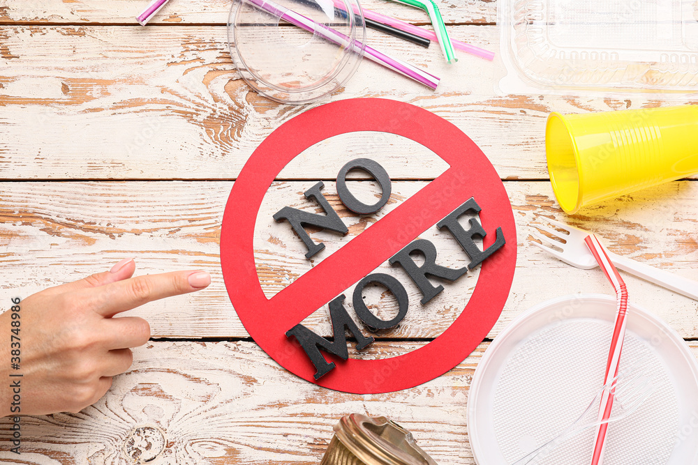 Female hand, plastic tableware and stop sign with text NO MORE on wooden background. Ecology concept