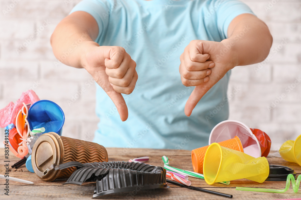 Woman with plastic garbage showing thumb-down gesture at table. Ecology concept