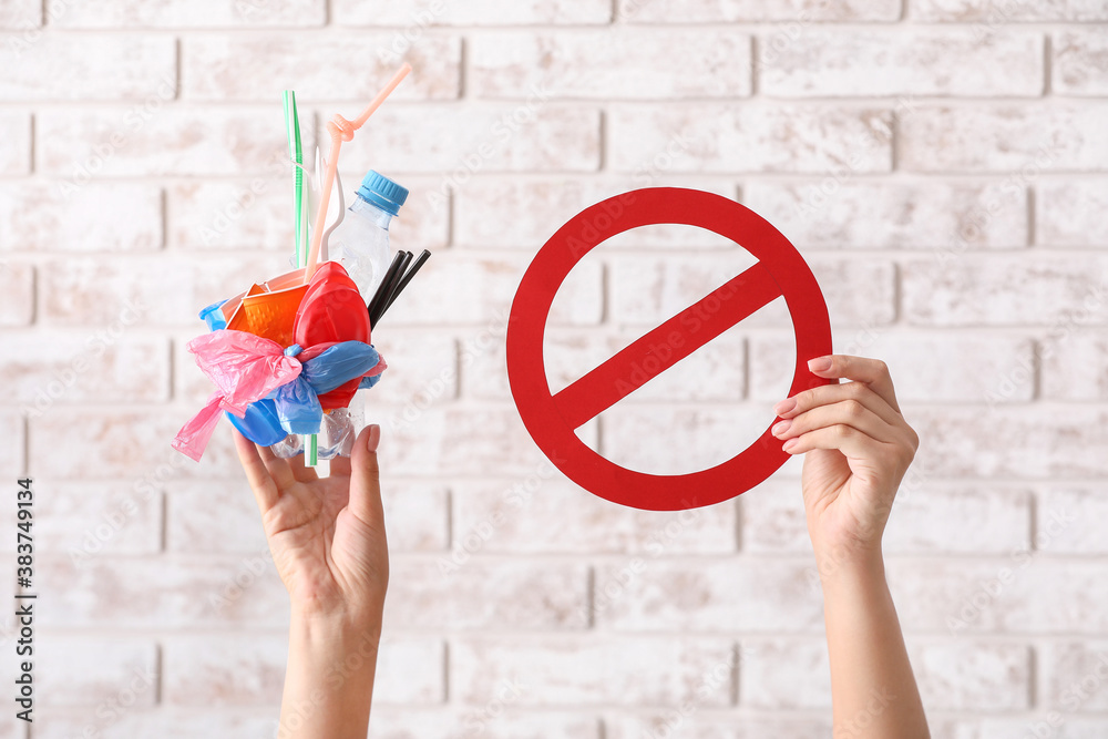 Female hands with plastic garbage and stop sign on brick background. Ecology concept