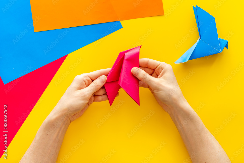 Female hands folding sheet of paper - origami bird. Overhead view