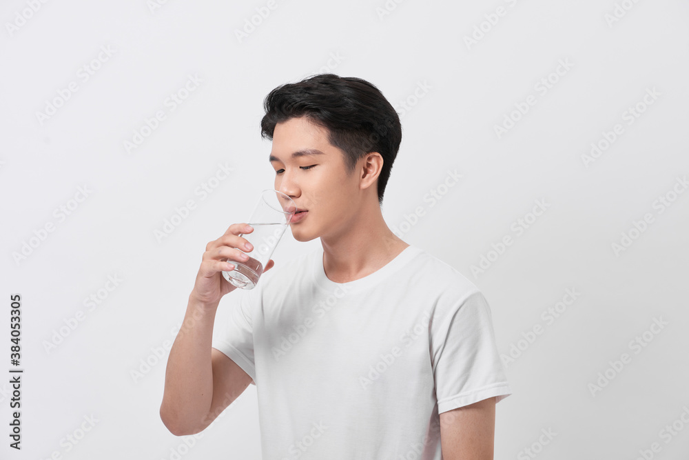 A man in a t-shirt and trousers on a white background drinking water from a glass