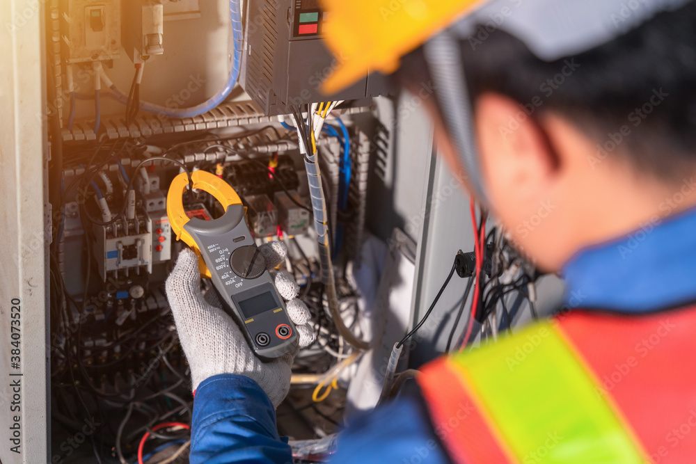 Digital clamp meter in hands of electrician close-up against background of electrical wires and rela