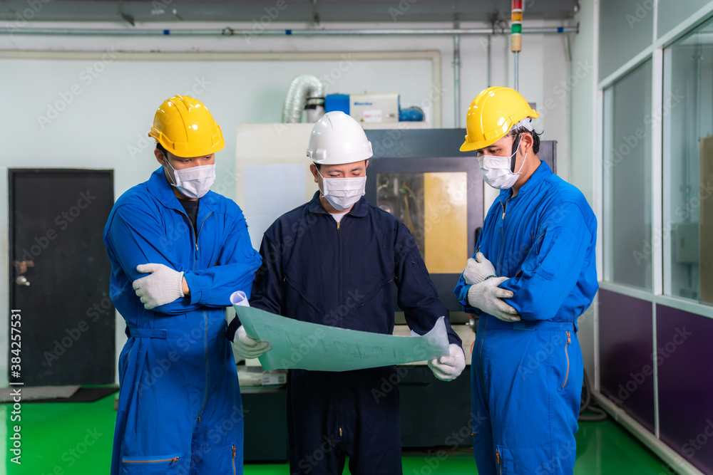 Asian industrial engineers and worker in hard hats discuss product line in blueprint and make showin