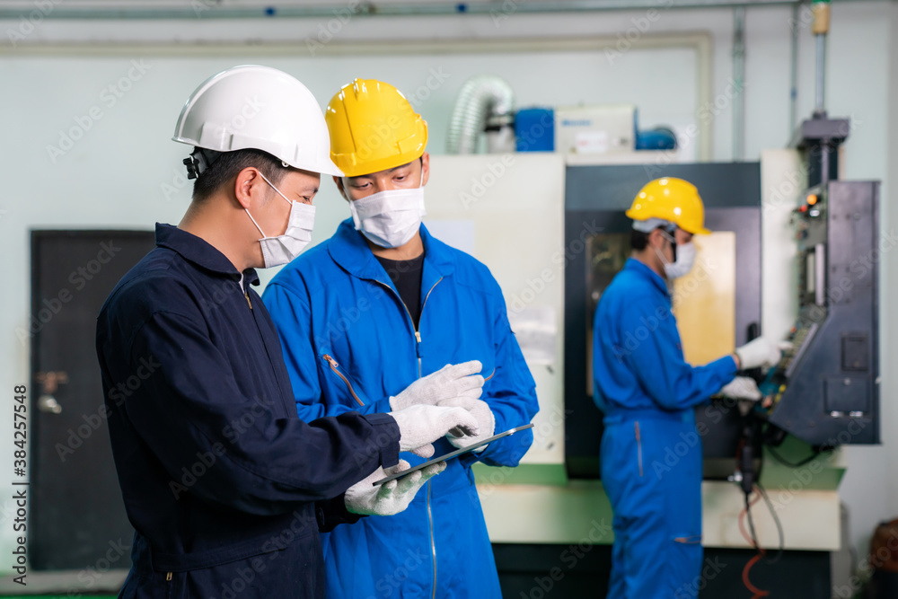 Asian industrial engineers and worker in hard hats discuss product line while using digital tablet a