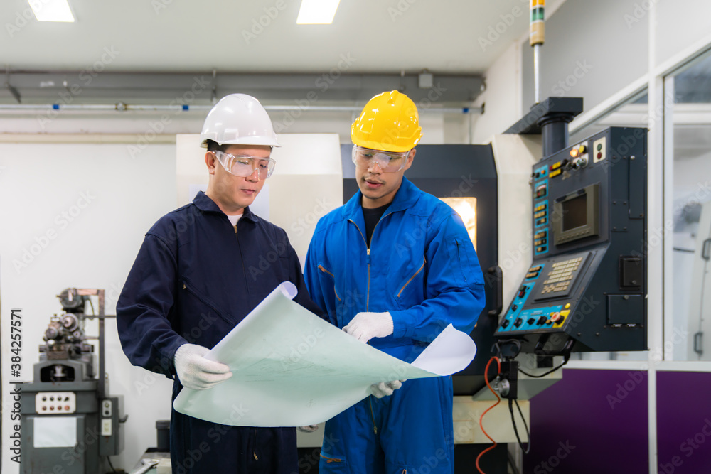 Asian industrial engineers and worker in hard hats discuss product line in blueprint and make showin