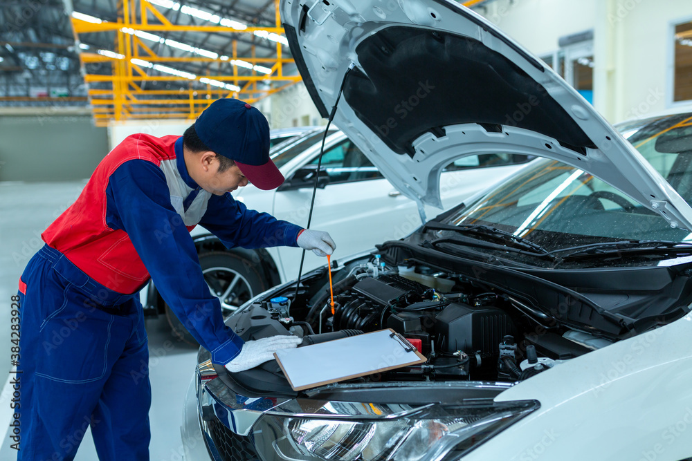 Auto mechanic checking car engine oil in car auto repair service center.